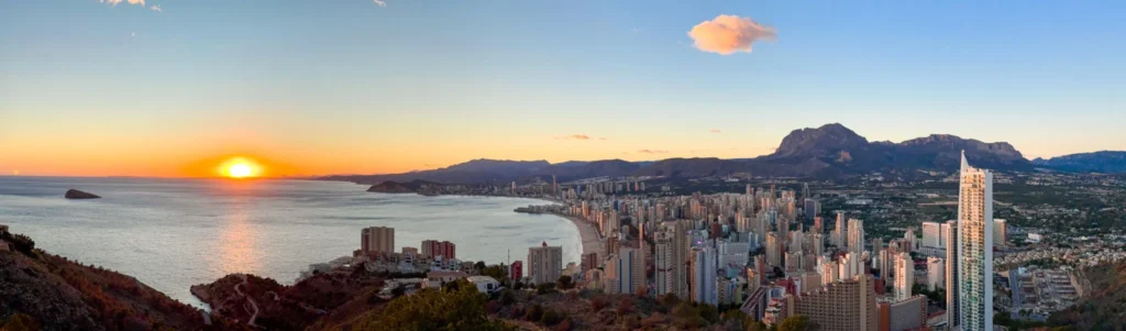Vista panorámica de Benidorm al atardecer desde Sierra Helada, con el mar Mediterráneo y sus rascacielos reflejando la luz del sol