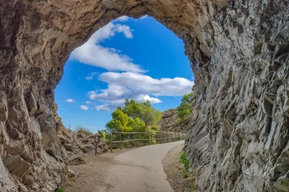 Túnel en la ruta al Faro del Albir dentro del Parque Natural de la Serra Gelada, con el camino curvado y el cielo azul enmarcado por la roca.
