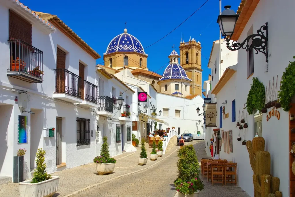 Calle típica del casco antiguo de Altea con las cúpulas azules de la iglesia al fondo.