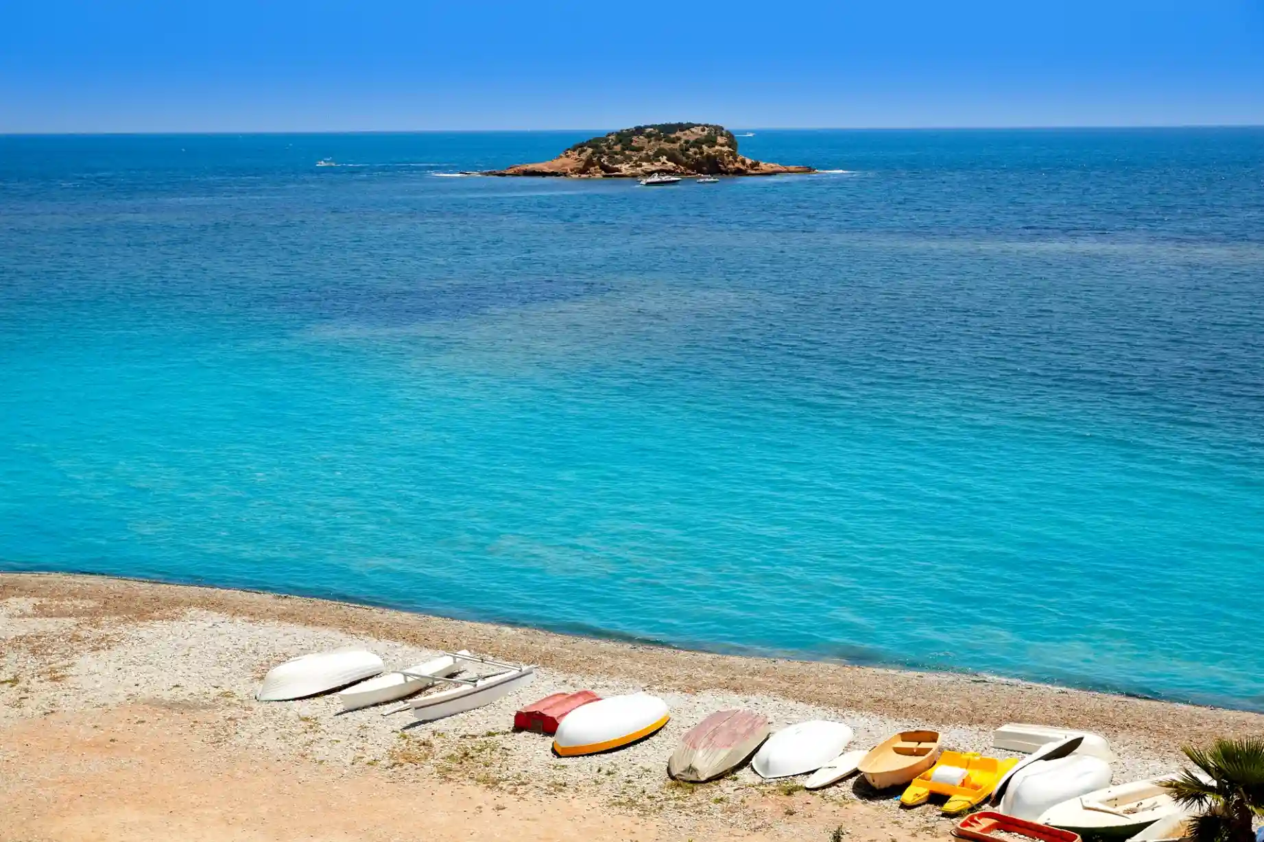 Isleta de la Olla en Altea vista desde la orilla, con aguas turquesas y embarcaciones en la playa