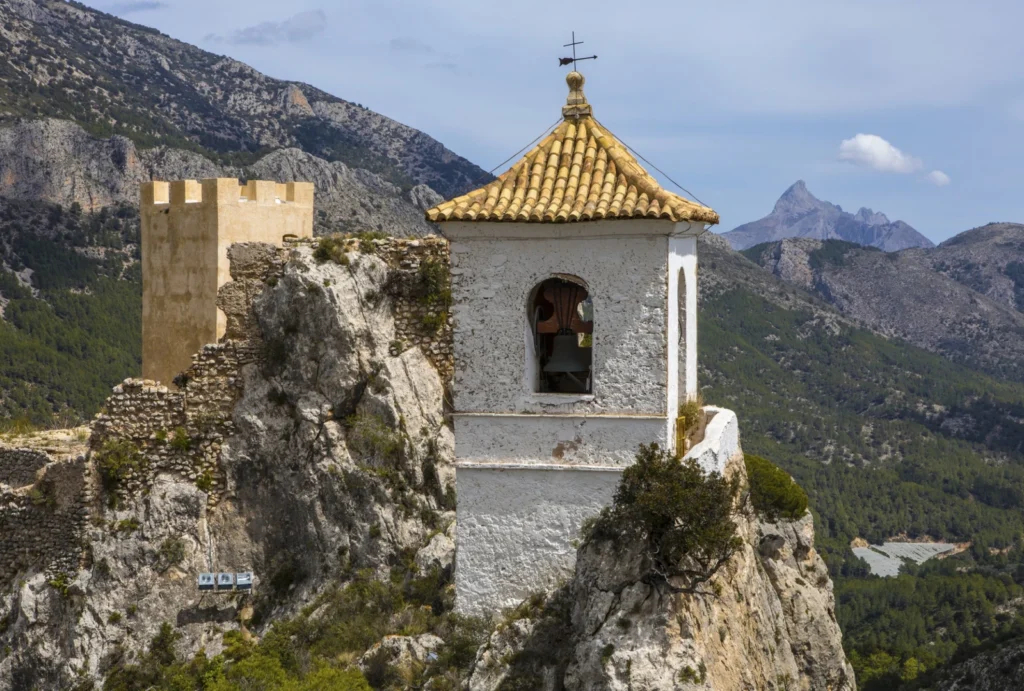 Campanario del Castillo de San José en Guadalest sobre un acantilado con las montañas de la Marina Baixa al fondo