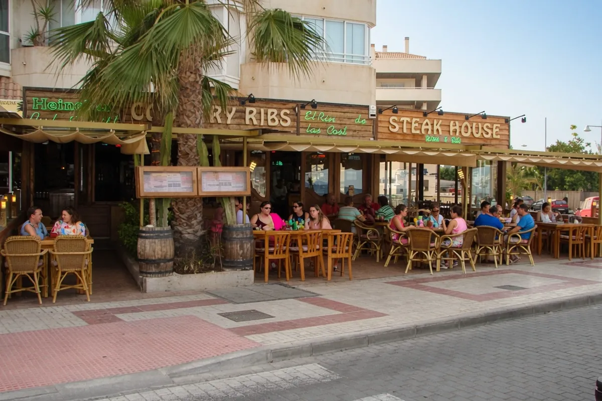 Terraza llena de gente en el restaurante Country Ribs Steak House, con turistas disfrutando de una comida al aire libre bajo el porche en un día soleado de verano.