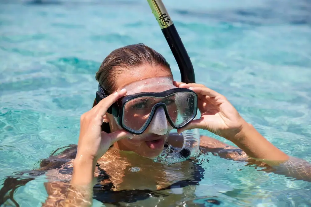 Mujer ajustando correctamente su máscara de snorkel bajo el agua, asegurándose de que selle bien alrededor de la cara. Demostración práctica para principiantes.