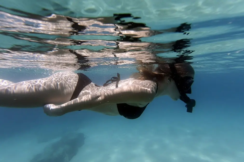 Mujer con bikini negro haciendo snorkel en la superficie del mar, nadando relajada con la cara sumergida y respirando por el tubo del snorkel.